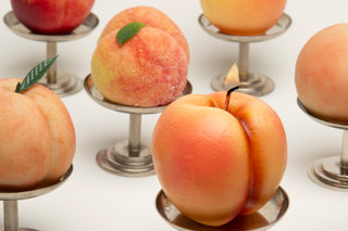 Sweetgreen x Gohar Peach Candle lit on a pedestal among other faux peaches.