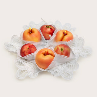 Sweetgreen x Gohar Peach Candle lit in a doily among other faux peaches.