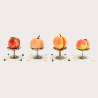 Sweetgreen x Gohar Peach Candle lit on a pedestal in a row with other faux peaches.